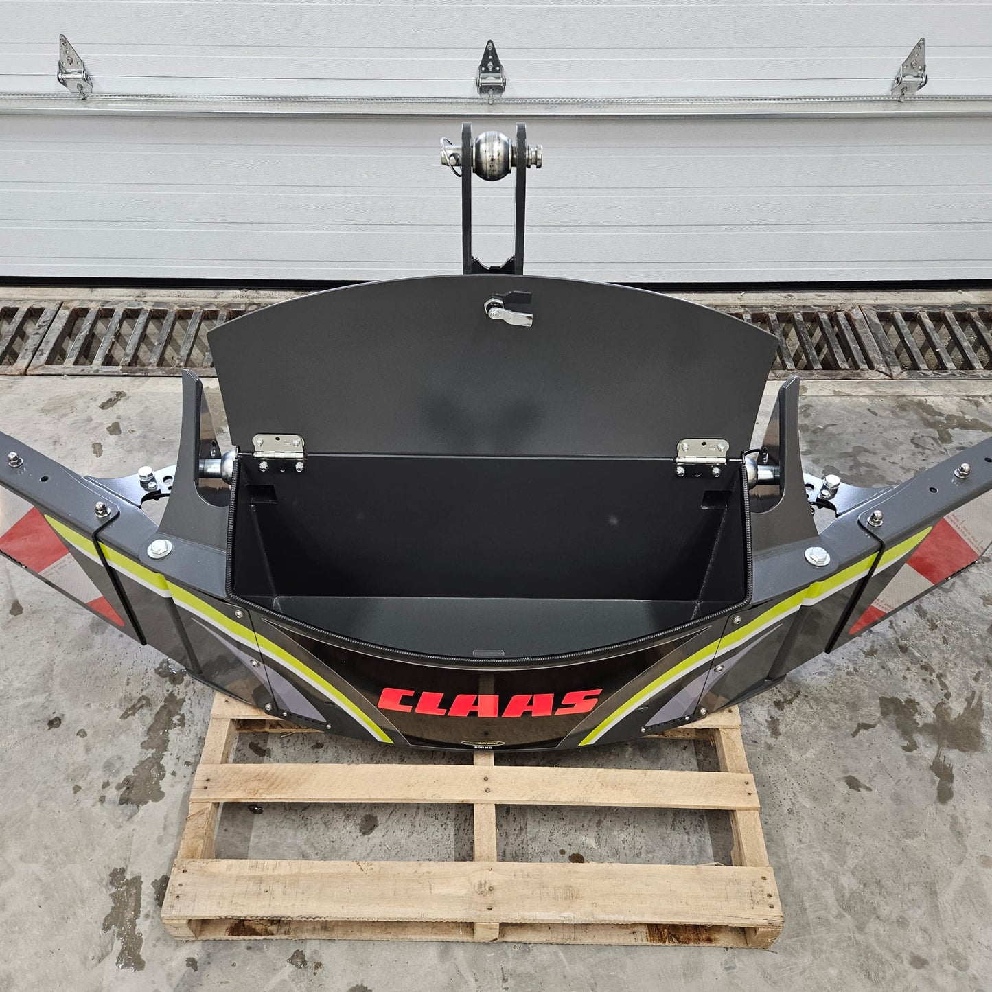 A CLAAS metal storage box sits open on a wooden pallet in front of a white garage door, showing its empty interior—ideal for storing your CLAAS TractorBumper 800KG or related accessories.