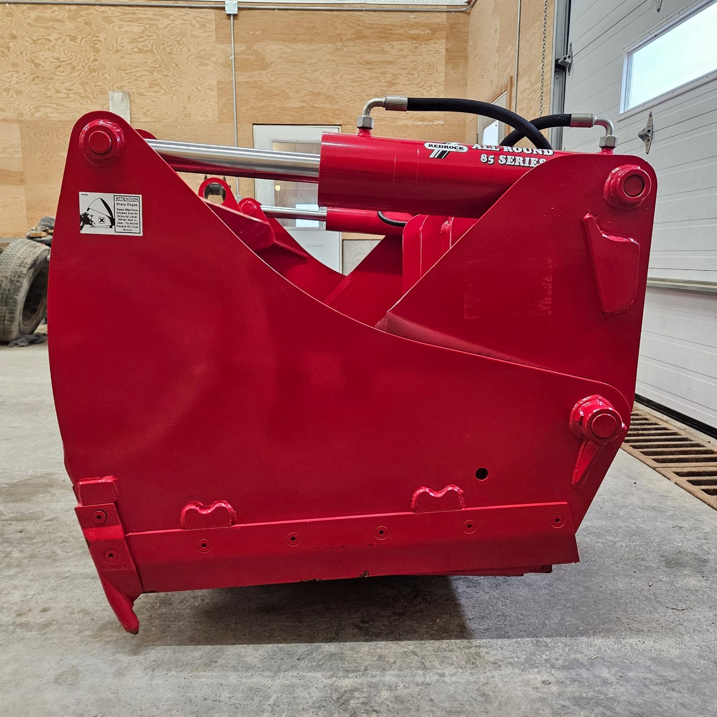 An UNUSED REDROCK Shear Bucket 200 (6’6”) hydraulic attachment sits on a concrete floor in a workshop with wood-paneled walls and a white garage door in the background.