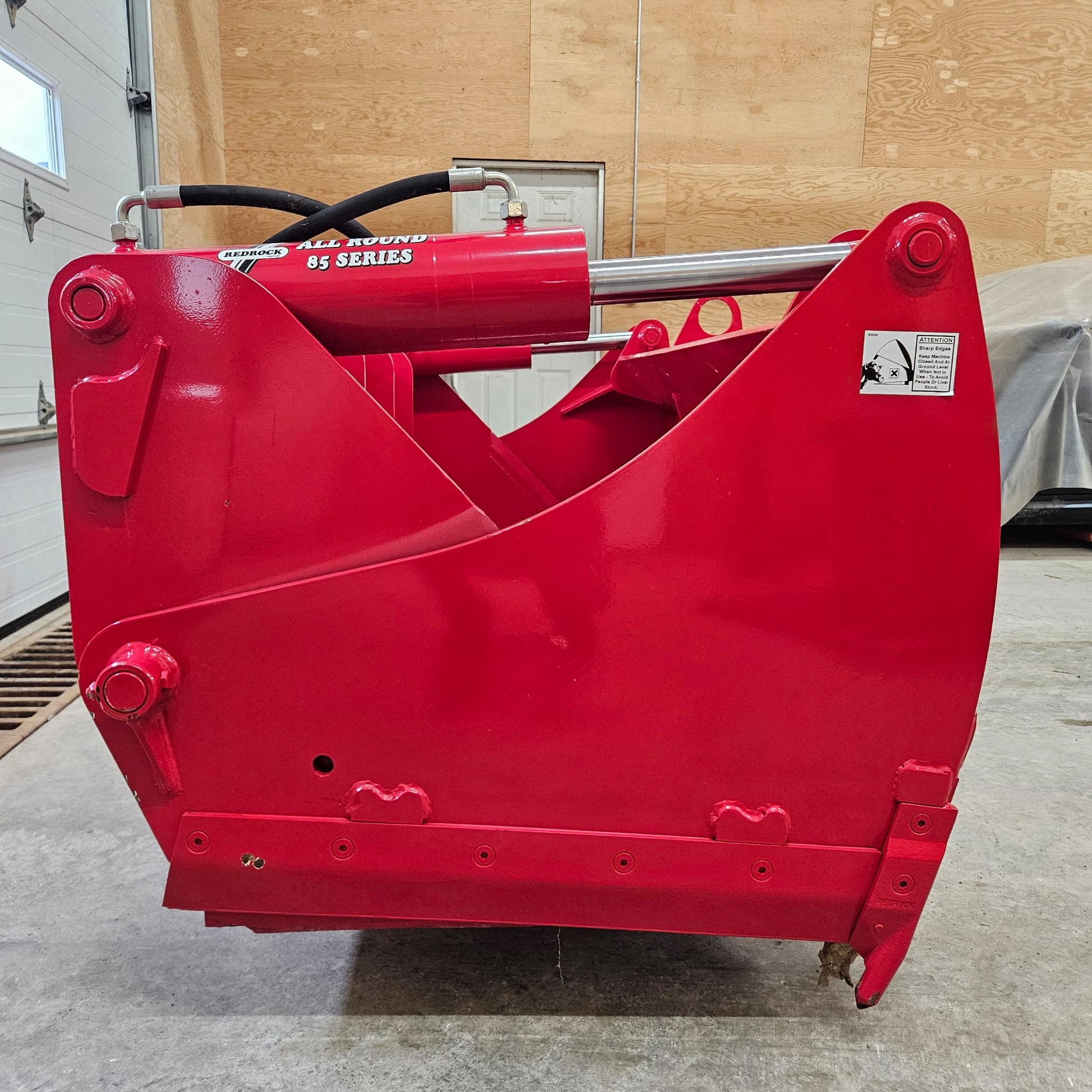 A REDROCK Shear Bucket 200 (6'6") | UNUSED, bright red and heavy-duty, sits indoors on a concrete floor, with wooden walls and a garage door visible in the background.