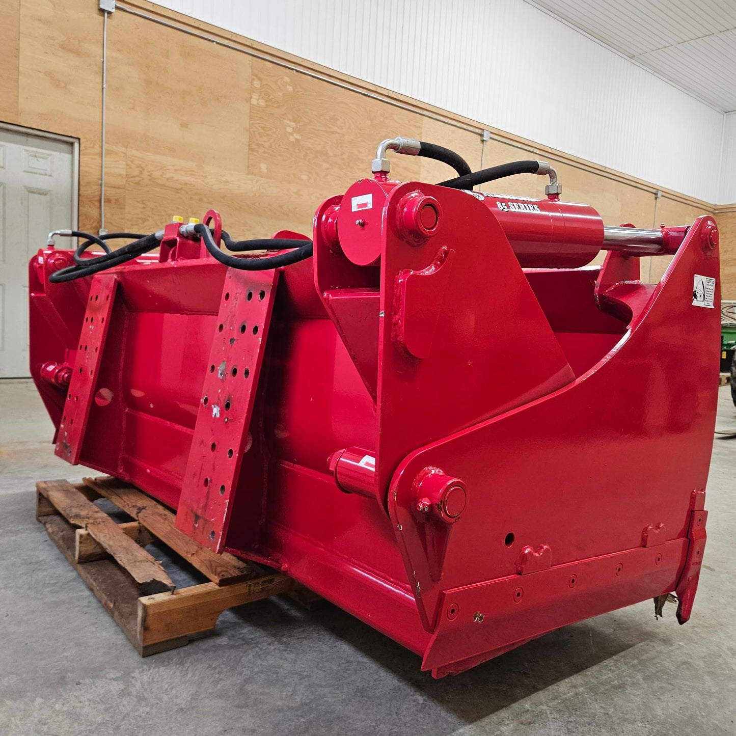 An UNUSED REDROCK Shear Bucket 200 (6'6"), featuring hydraulic components and a durable red frame, sits on a pallet in a warehouse—ideal for efficient silage cutting.